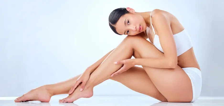 A woman seated on the floor, legs extended outward, thinking about the benefits of urea for skin hydration